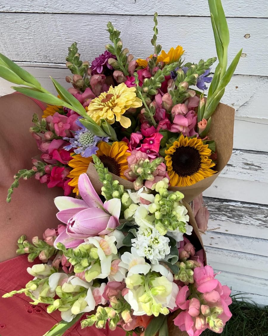 A lush handmade bouquet of sunflowers, snapdragons, zinnias, and tulips wrapped in kraft paper